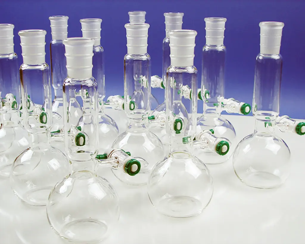 A dozen saponification flasks lined up on a table. The flasks are unique with a round bottom and long neck,