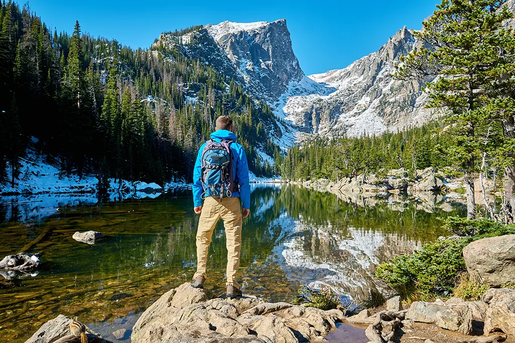 Future glassblower dreaming about the job opportunities. Young man stands on a rock over a lake and looks up at a snow-capped mountain. How high can your career take you?