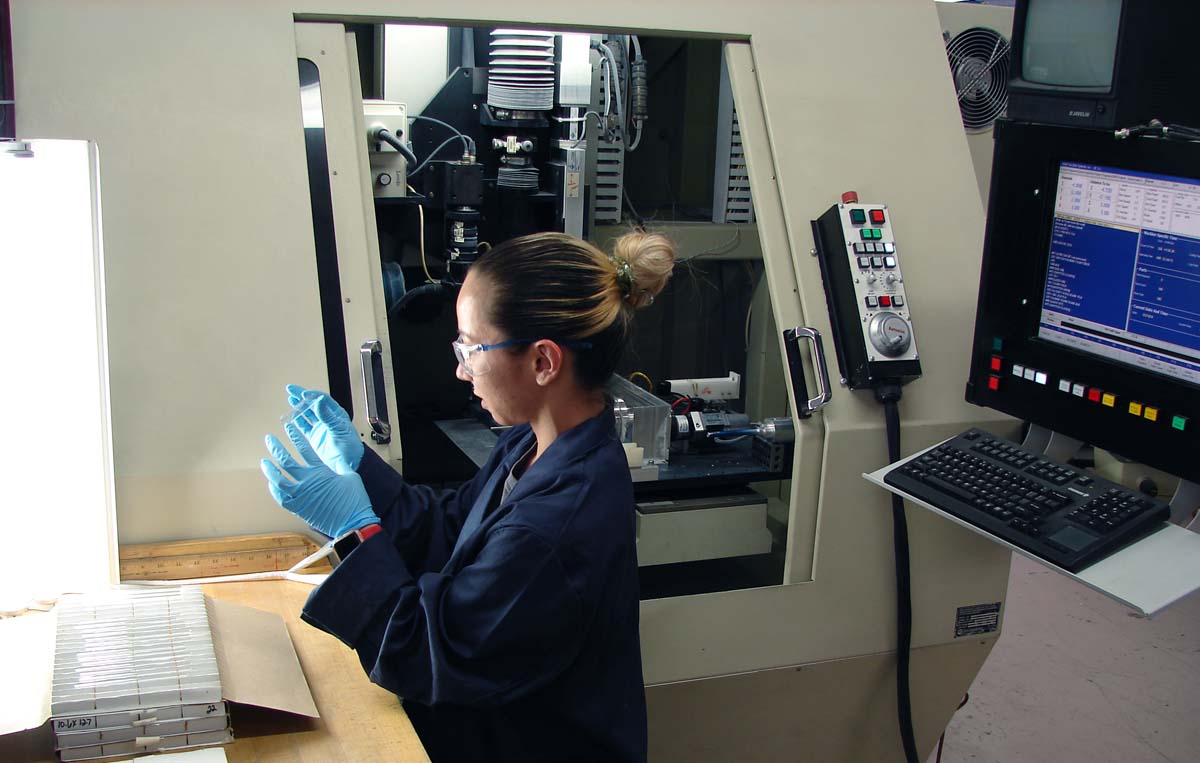 The smooth finish of a glass lab slide is inspected by a glass manufacturing technician.